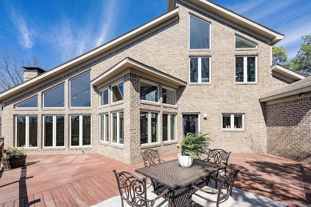 back of house featuring brick siding, outdoor dining space, a deck, and a chimney
