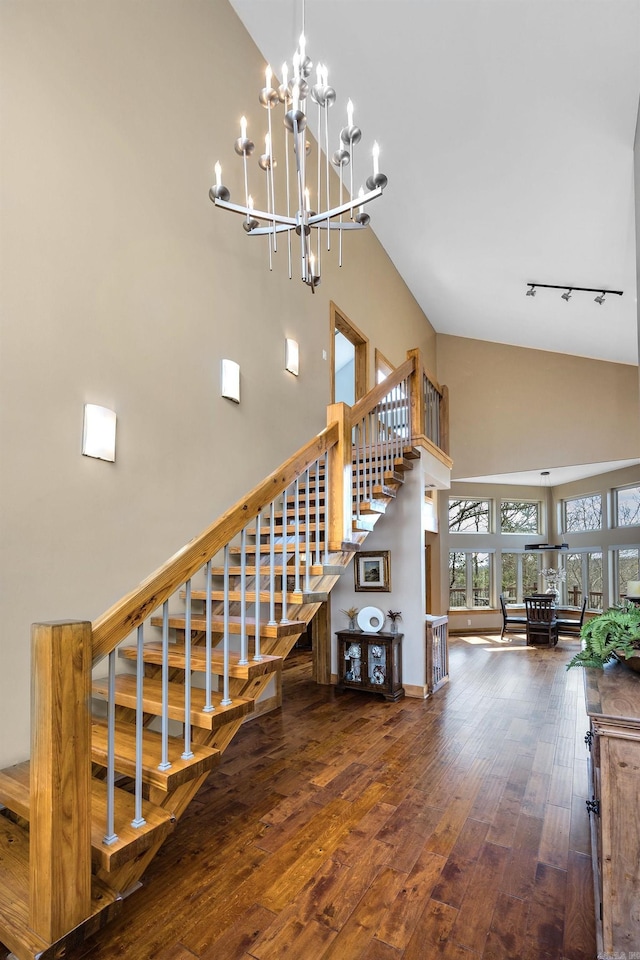 stairs featuring high vaulted ceiling, rail lighting, a notable chandelier, and hardwood / wood-style flooring