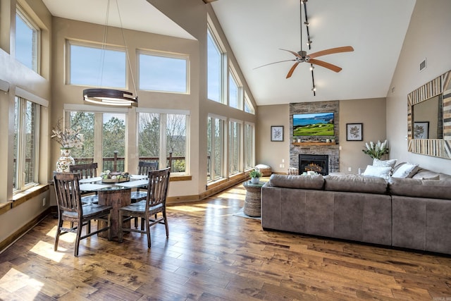 living room with baseboards, a stone fireplace, ceiling fan, high vaulted ceiling, and wood finished floors