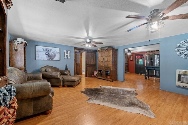 living area featuring heating unit, a ceiling fan, a textured ceiling, and wood finished floors