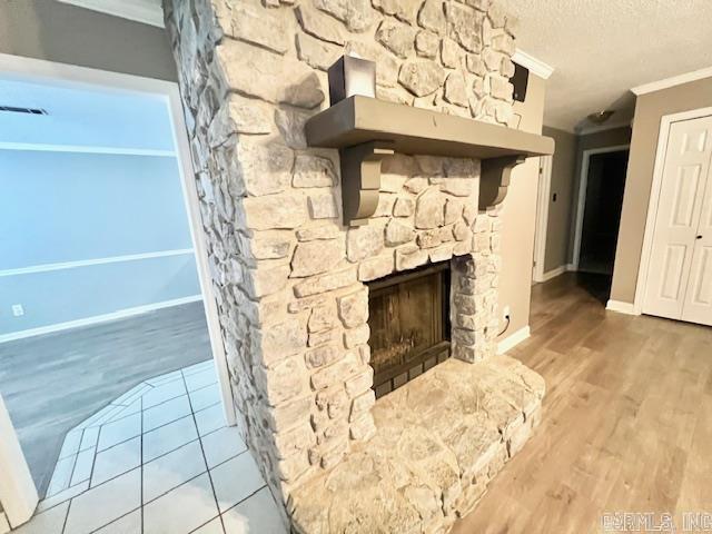 unfurnished living room featuring crown molding, a fireplace, wood finished floors, a textured ceiling, and baseboards