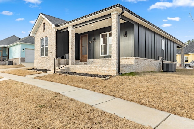 view of front facade featuring cooling unit, board and batten siding, a front yard, brick siding, and a garage