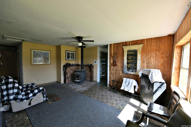 living area with a ceiling fan, wood walls, baseboards, and a wood stove