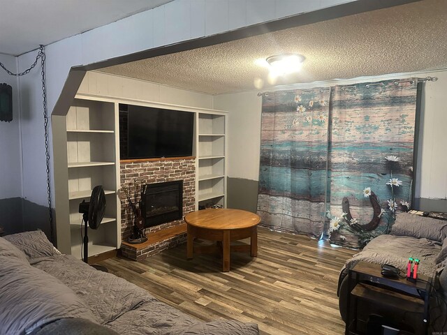 living area with a textured ceiling, wood finished floors, and a brick fireplace