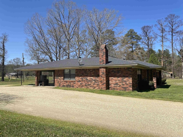 view of front facade with driveway, a front yard, brick siding, an attached carport, and a chimney