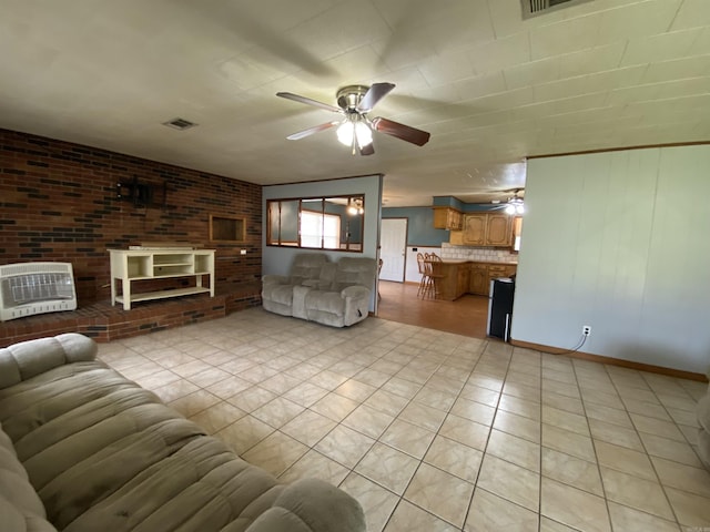 unfurnished living room featuring light tile patterned floors, brick wall, visible vents, heating unit, and a ceiling fan