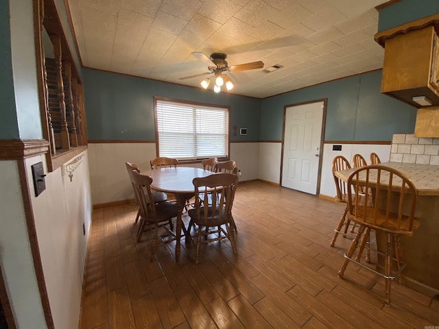 dining area featuring a ceiling fan, a wainscoted wall, dark wood-type flooring, and visible vents
