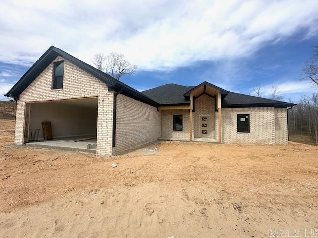 rear view of house featuring dirt driveway, brick siding, and a garage