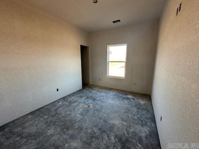 spare room featuring a textured wall, concrete floors, and visible vents