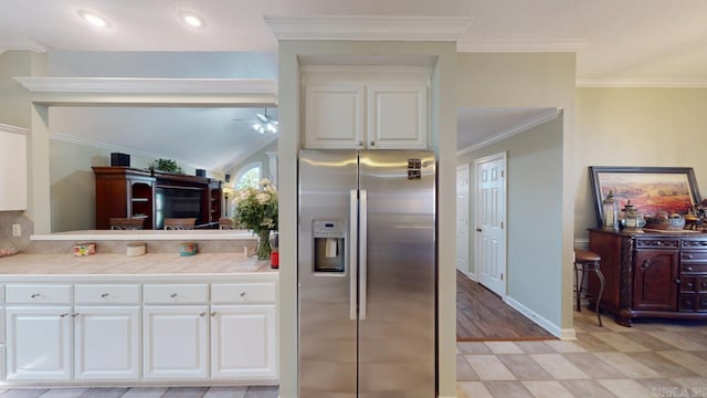 kitchen with vaulted ceiling, crown molding, stainless steel fridge, white cabinets, and ceiling fan