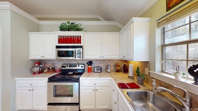 kitchen with tasteful backsplash, ornamental molding, stainless steel appliances, a sink, and white cabinets
