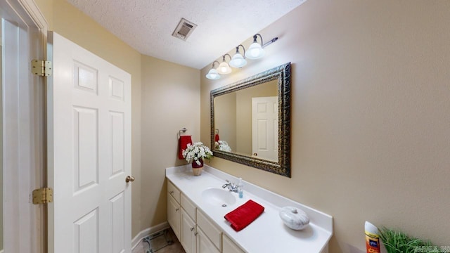 bathroom featuring vanity, a textured ceiling, baseboards, and visible vents