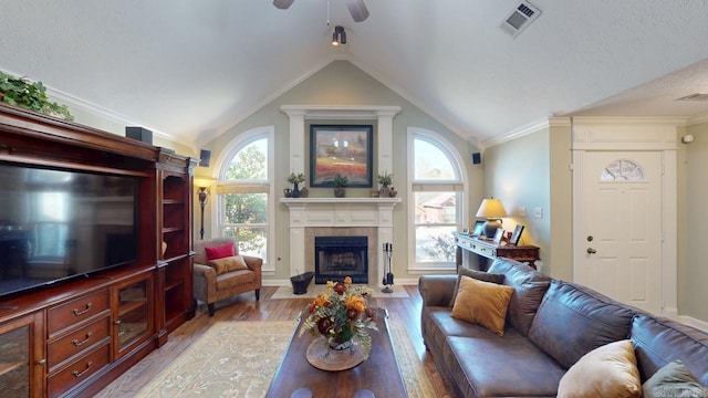 living room with a tile fireplace, wood finished floors, lofted ceiling, visible vents, and ceiling fan