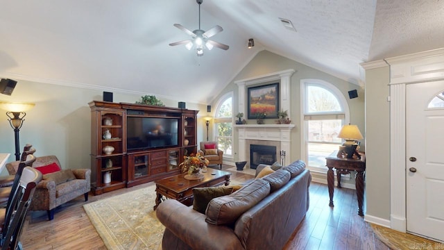 living room with lofted ceiling, visible vents, a tiled fireplace, ceiling fan, and wood finished floors