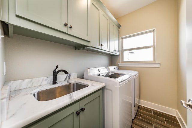 clothes washing area featuring a sink, wood finish floors, baseboards, washer and dryer, and cabinet space