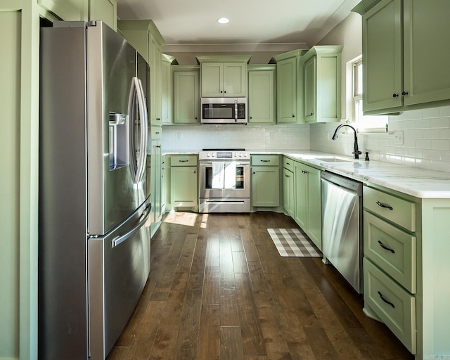 kitchen featuring green cabinetry, a sink, backsplash, appliances with stainless steel finishes, and dark wood-style flooring