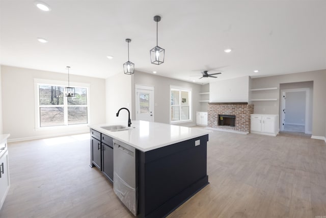 kitchen featuring ceiling fan, stainless steel dishwasher, light wood-style flooring, a sink, and a brick fireplace