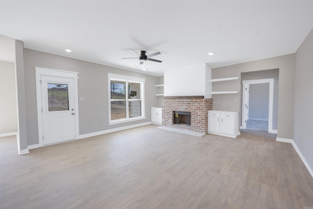 unfurnished living room with ceiling fan, light wood-type flooring, recessed lighting, a brick fireplace, and baseboards