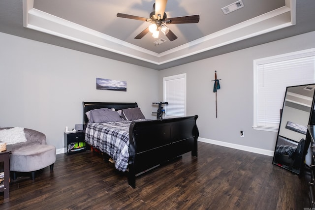 bedroom with wood finished floors, a tray ceiling, baseboards, and visible vents