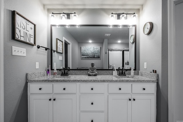 bathroom featuring a textured wall, double vanity, a sink, and a stall shower