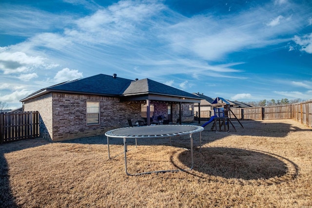 rear view of house featuring a playground, a trampoline, a fenced backyard, brick siding, and a lawn