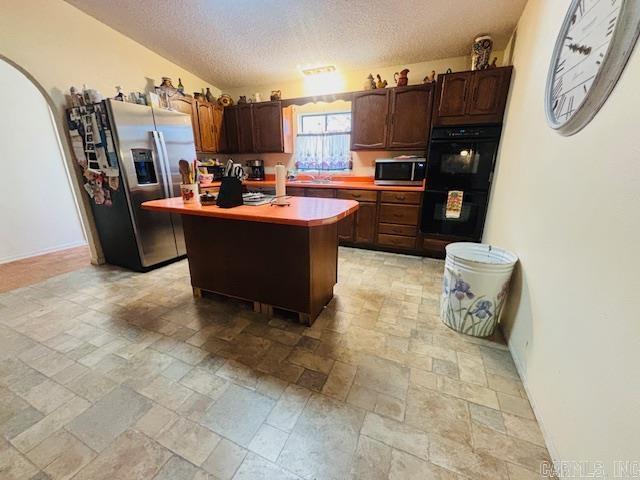 126 Dallas Ln, Mena, AR 71953 - kitchen with a center island, light countertops, a textured ceiling, stainless steel appliances, and stone tile floors
