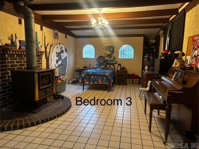 126 Dallas Ln, Mena, AR 71953 - bedroom with light tile patterned flooring, a wood stove, beamed ceiling, and a notable chandelier
