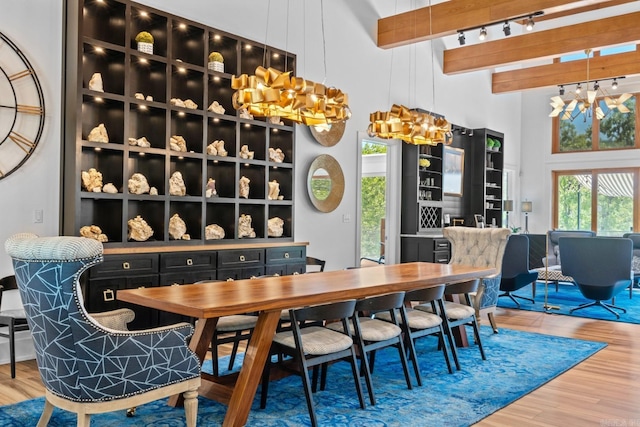 dining room featuring rail lighting, wood finished floors, beam ceiling, a high ceiling, and a notable chandelier
