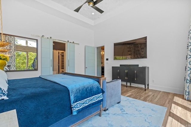 bedroom featuring baseboards, wood finished floors, a ceiling fan, a tray ceiling, and a high ceiling
