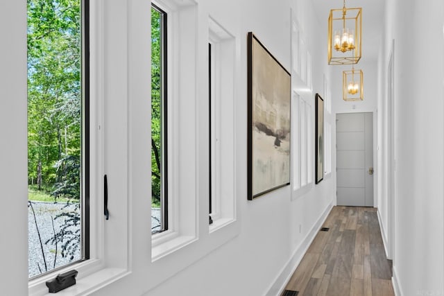 hallway with baseboards, dark wood-style floors, and a notable chandelier