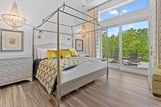 bedroom featuring access to exterior, a notable chandelier, wood finished floors, and a towering ceiling