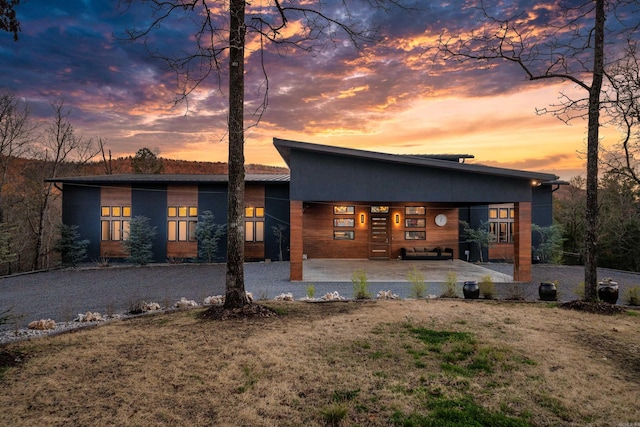 back of property with a lawn, an attached carport, and gravel driveway