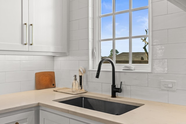 room details featuring white cabinetry, a sink, backsplash, and light stone counters