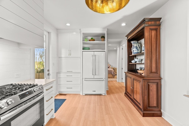 kitchen featuring stainless steel gas range, white cabinetry, open shelves, light wood-type flooring, and built in refrigerator
