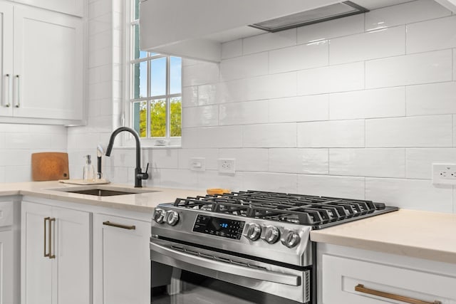 kitchen with decorative backsplash, white cabinets, a sink, and stainless steel gas range