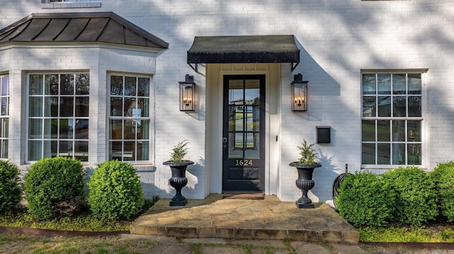 view of exterior entry featuring metal roof, a standing seam roof, and brick siding