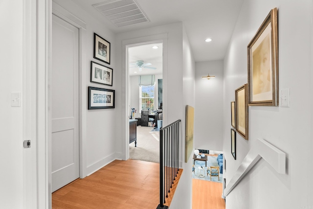 hallway with an upstairs landing, light wood-type flooring, baseboards, visible vents, and recessed lighting