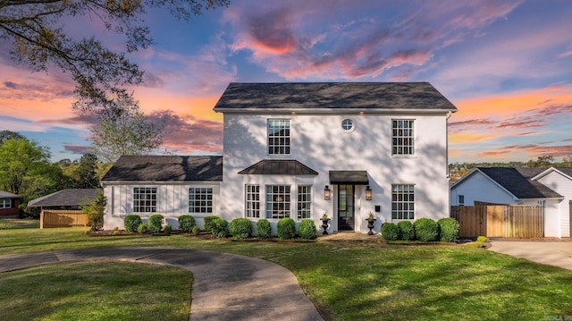 colonial home with stucco siding, fence, curved driveway, and a front yard