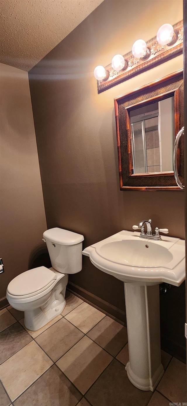 half bath with toilet, baseboards, and tile patterned flooring