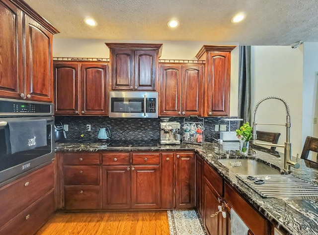 kitchen with a sink, dark stone countertops, decorative backsplash, and appliances with stainless steel finishes