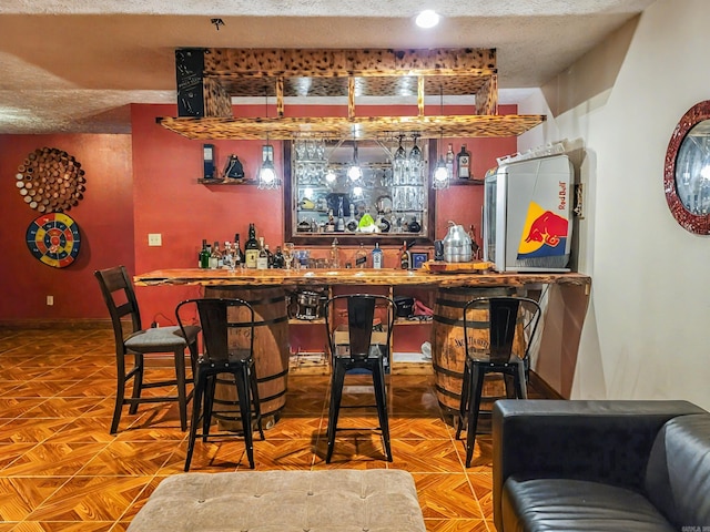 bar with a bar, baseboards, and a textured ceiling