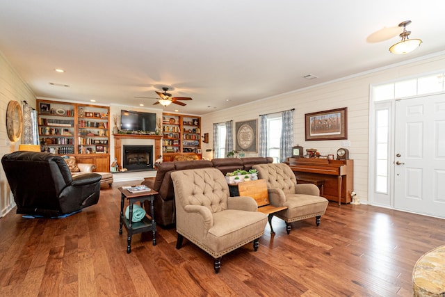 living area with recessed lighting, ornamental molding, a fireplace with raised hearth, ceiling fan, and wood finished floors