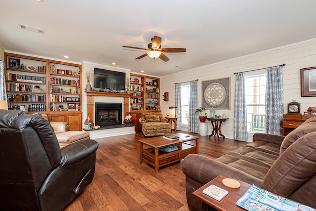 living area with visible vents, crown molding, a fireplace with raised hearth, ceiling fan, and wood finished floors