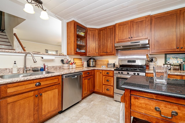 kitchen with stainless steel appliances, under cabinet range hood, a sink, light stone countertops, and brown cabinets