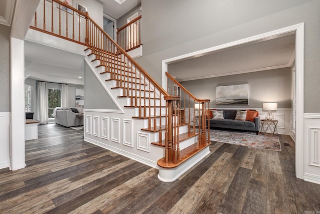 staircase with a wainscoted wall, a high ceiling, wood finished floors, a decorative wall, and ornamental molding