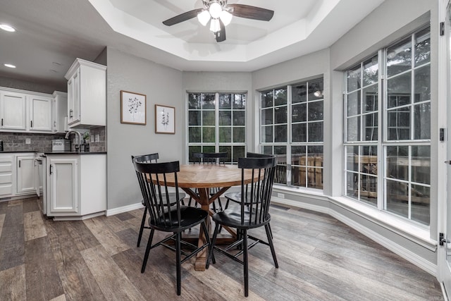 dining room with baseboards, dark wood finished floors, ceiling fan, and a raised ceiling