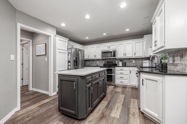 kitchen featuring stainless steel appliances, dark stone counters, dark wood-type flooring, white cabinetry, and a sink
