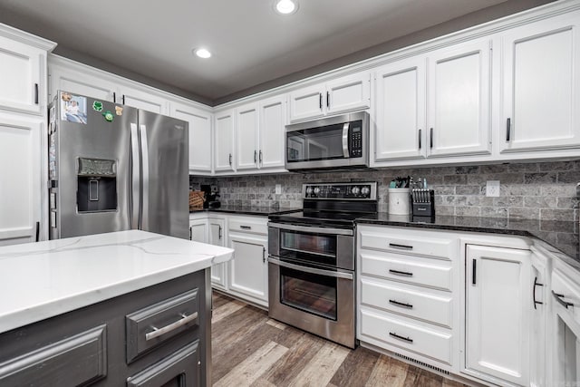 kitchen with tasteful backsplash, dark wood finished floors, dark stone counters, white cabinets, and appliances with stainless steel finishes