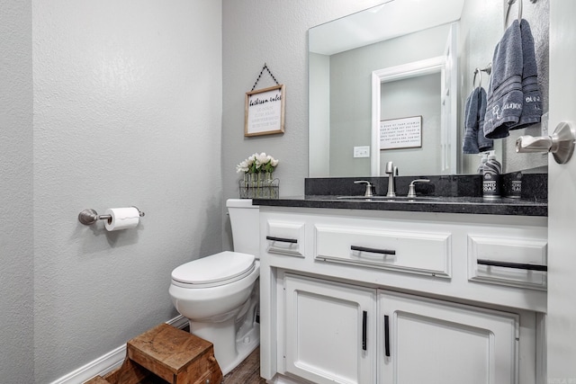 bathroom featuring toilet, vanity, and a textured wall