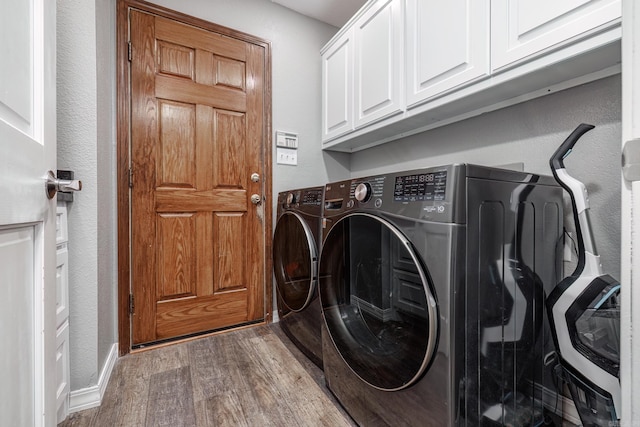 laundry room featuring washer and clothes dryer, wood finished floors, cabinet space, and a textured wall